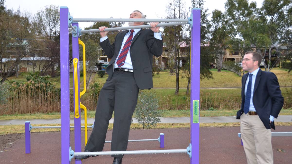 Inverell Shire mayor Paul Harmon tries a chin-up on the new exercise equipment as MP Adam Marshall looks on.