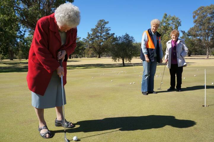 GOLFING GRANT: Grace McGufficke tries her luck on the putting green while HACC volunteer Colleen Makim and resident Rae Morris look on.
