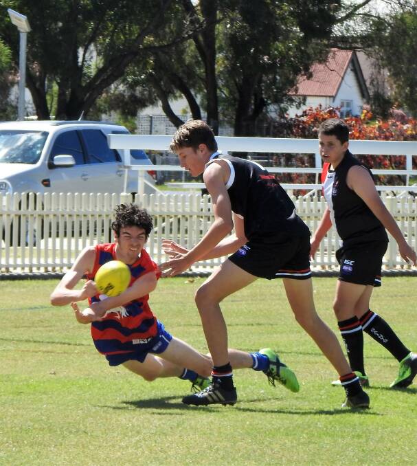 FIRST GAME OF SEASON: Roosters James Vallander coughs up the ball under pressure from Saints Juniors Captain Will Mozzell and Cody McGillivray in support at Varley Oval in Inverell.