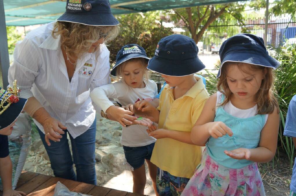 Kindamindi educator Lesley Tome shows some of the exciting green sand intended for the pathway with preschoolers Layla, Monty and Belinda.